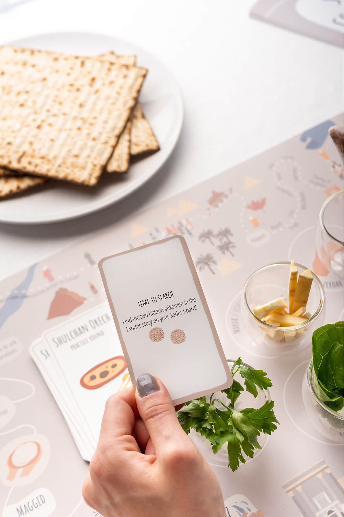 A hand holding the Time To Search Seder Card over the table
