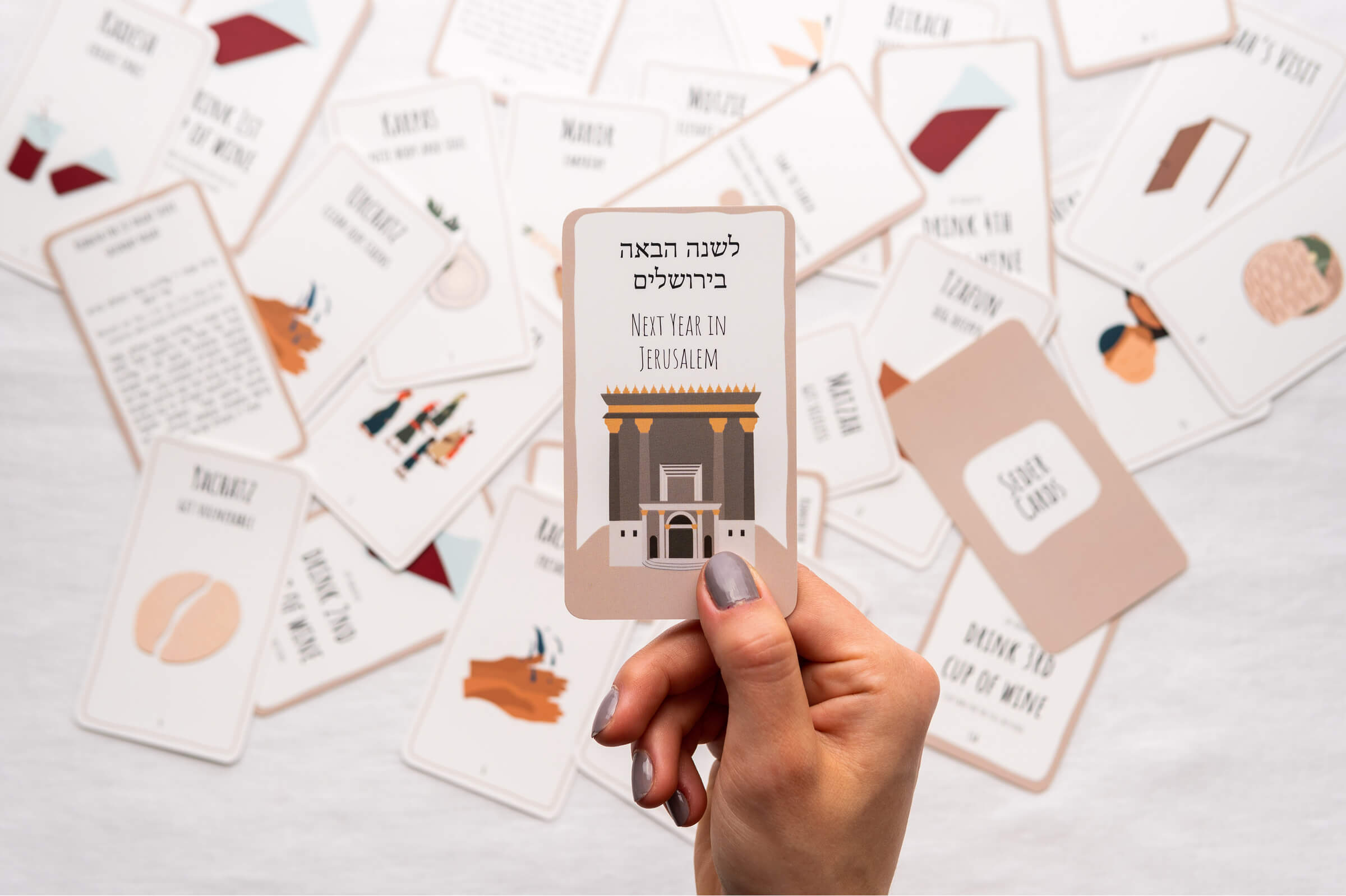 A hand holding the Next Year In Jerusalem Seder Card above a spread of cards