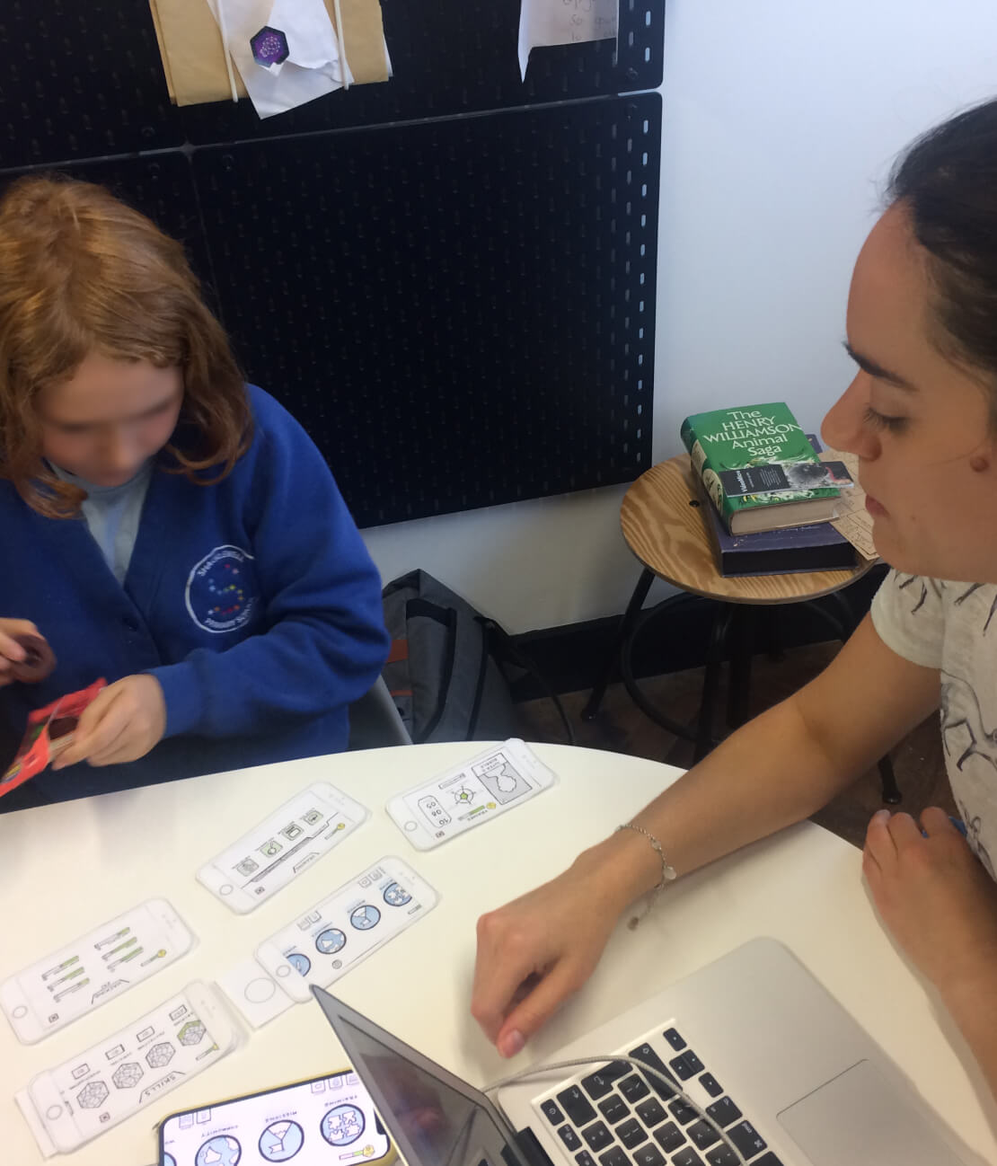 Paper prototype phone screens laid out on a table during a testing session with a child