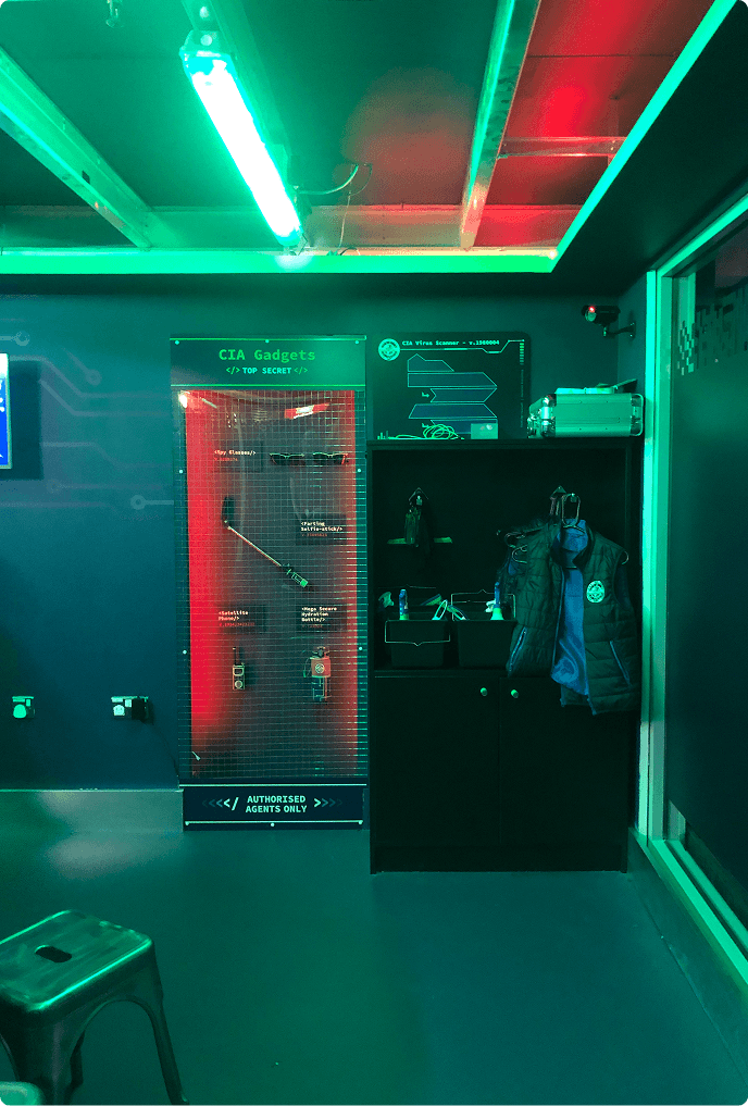 A CIA Gadgets display locker next to a cabinet holding an agent vest, lit in red and green
