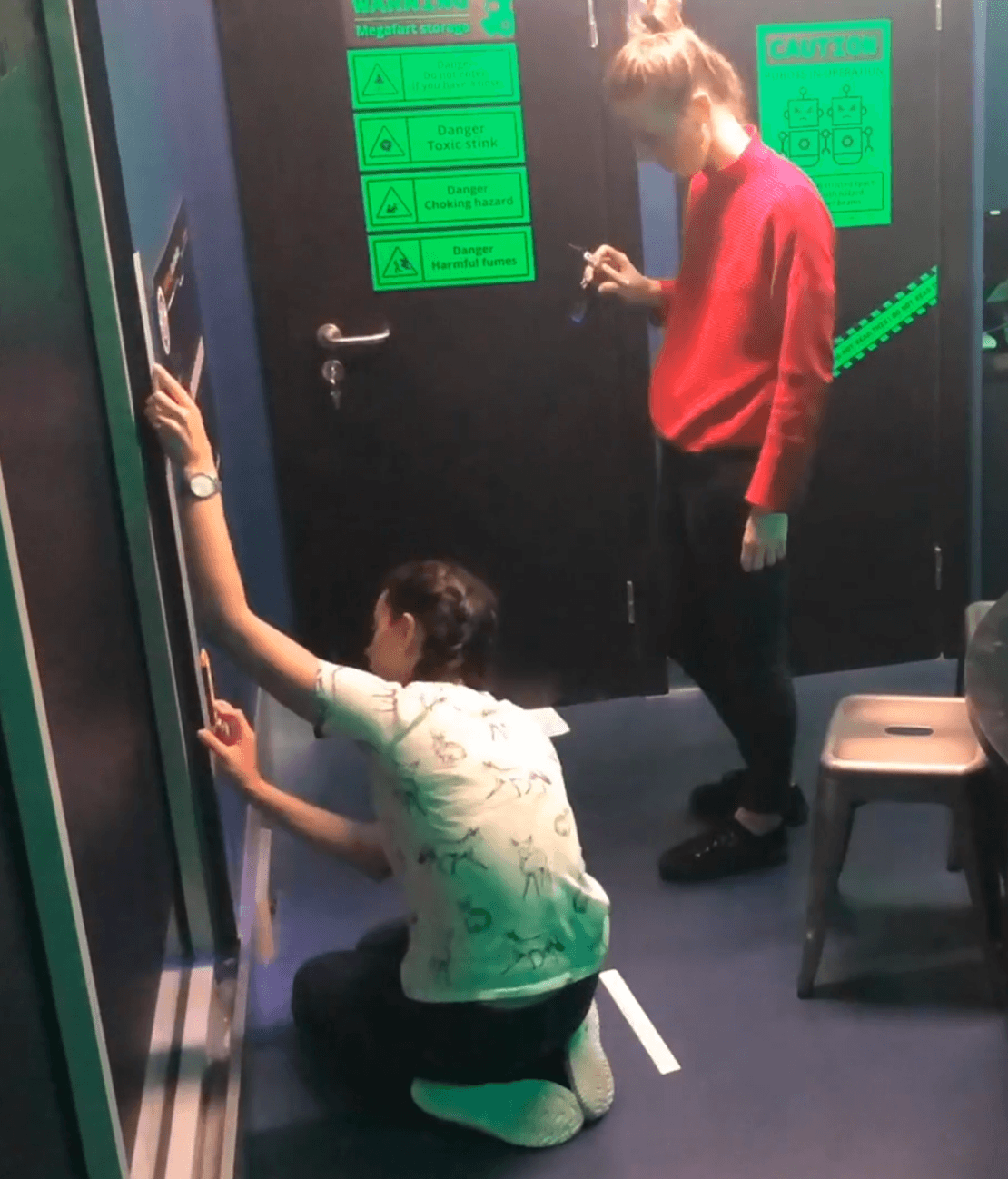 Two people mounting a warning sign to a dark panelled wall inside the unit during installation