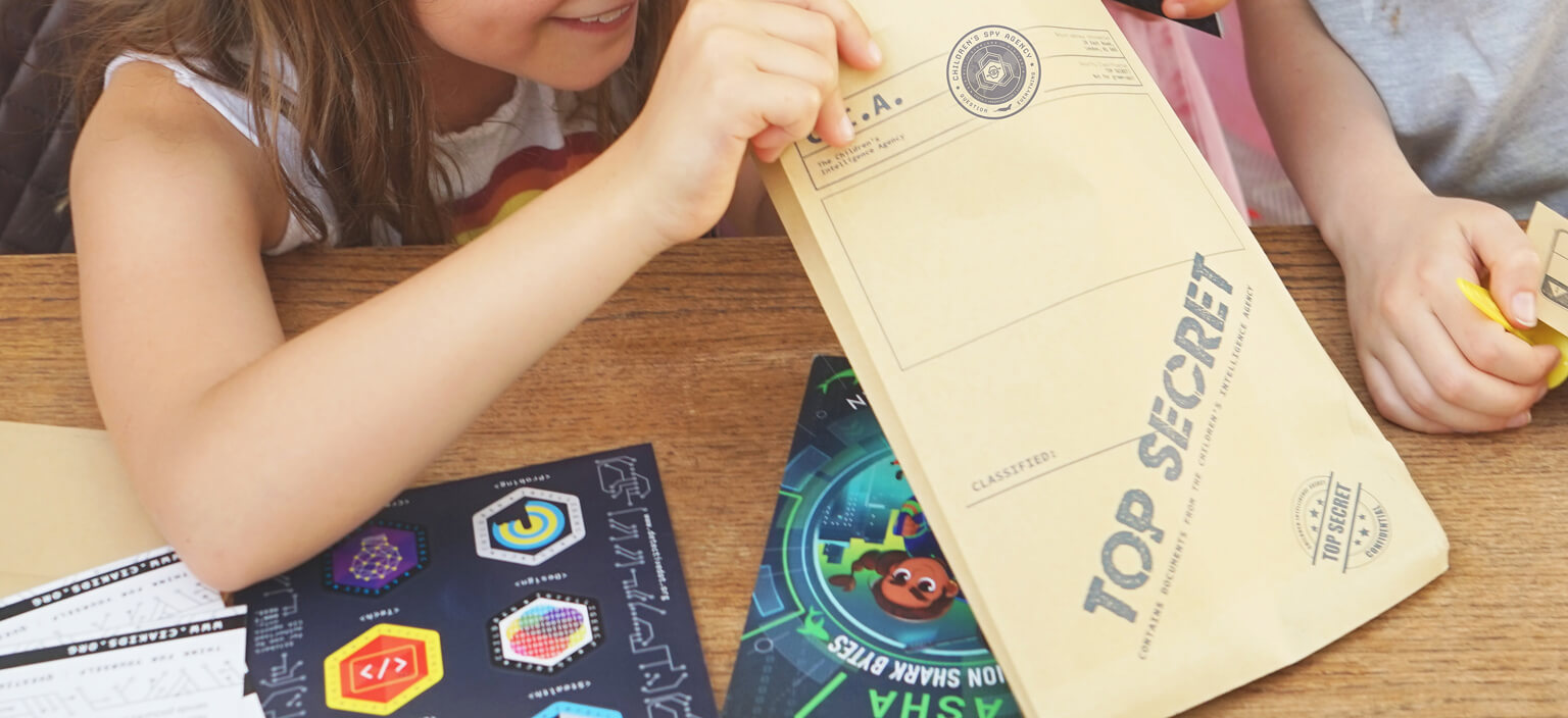 A child leaning over a table, opening a top-secret CSA envelope, with spy pack stickers and cards laid out beside it