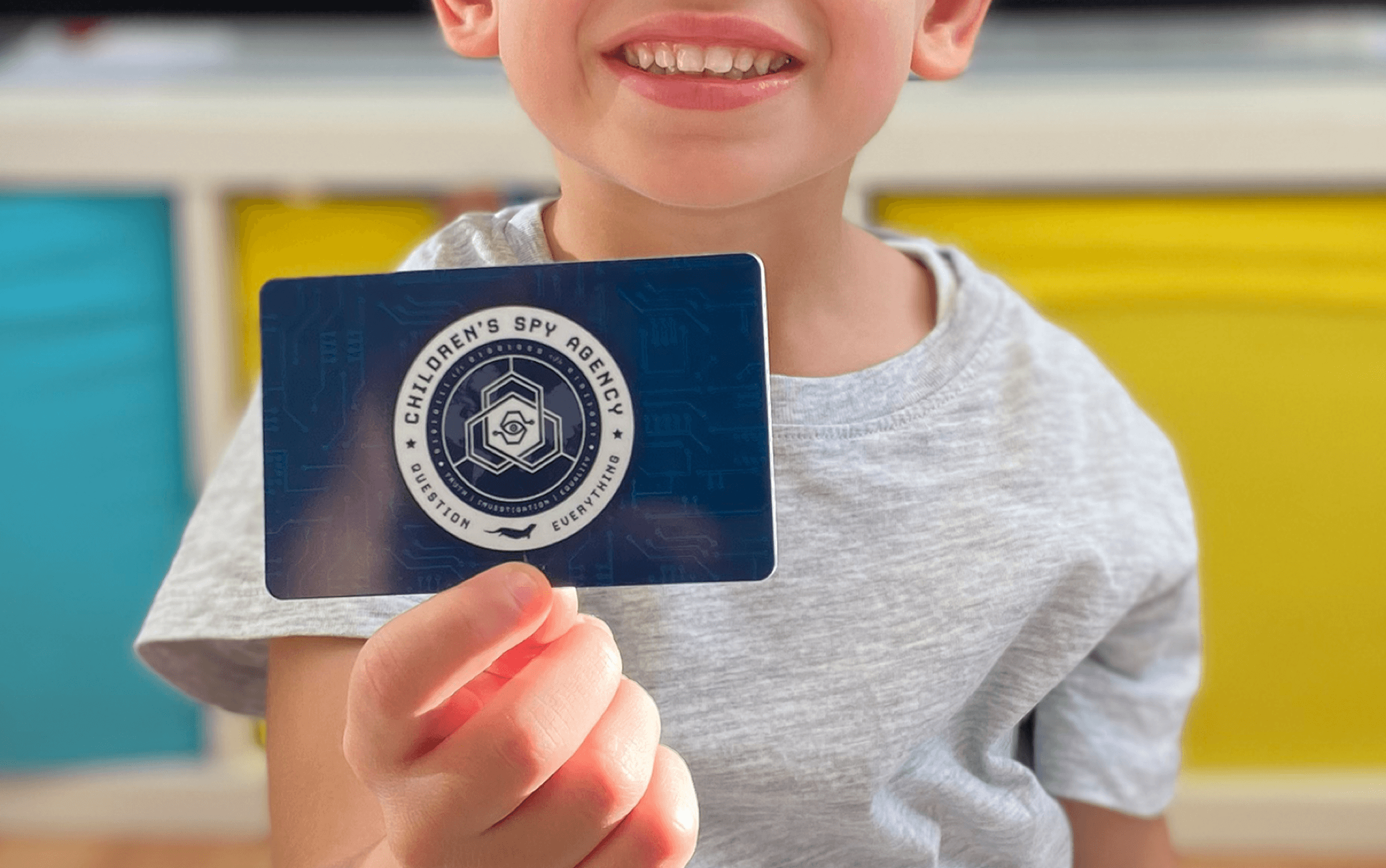 A child smiling and holding up their Children's Spy Agency membership card